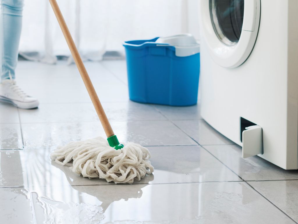 11 Common Types Of Plumbing Emergencies And How To Handle Them 7 A woman mopping leak from washing machine